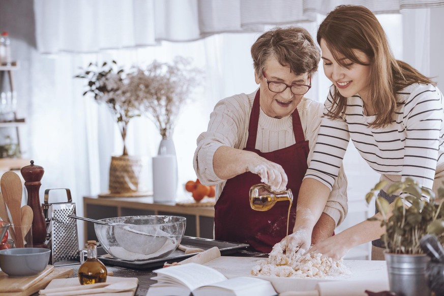 Grandmother helping her granddaughter make dough by adding olive oil