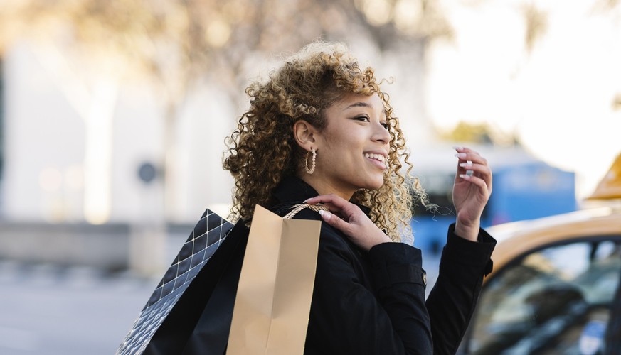 Pretty Hispanic woman with curly hair walking with shopping bags through the city,