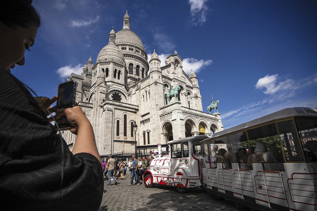 A tourist takes a picture of the Sacre Coeur basilica in the Montmartre district in Paris, France, Monday, Aug. 4, 2025. (AP Photo/Aurelien Morissard)