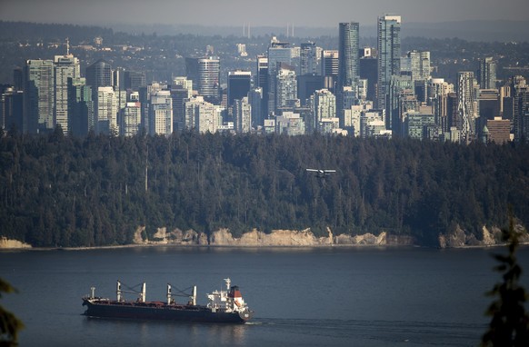 A bulk carrier cargo ship travels into port as a Harbour Air seaplane flies towards Stanley Park and the downtown skyline, in Vancouver, British Columbia on Wednesday, July 27, 2022. (Darryl Dyck/The  ...