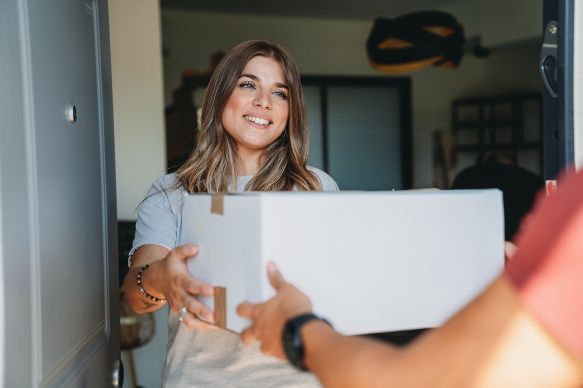 Delivery man is giving a box to a woman. A courier is making a delivery to a customer at her home.
