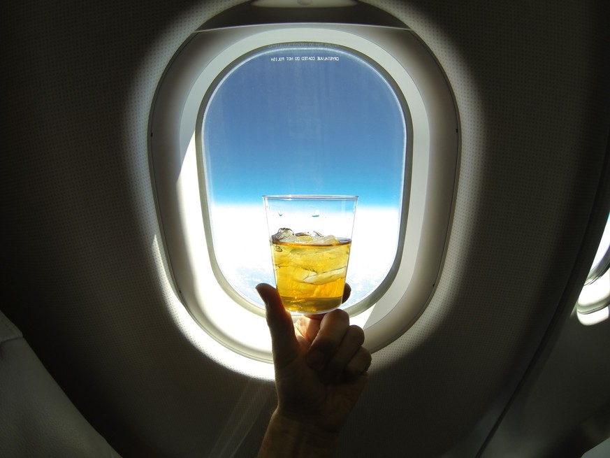 Refreshing glass of ice tea (or alcohol mix) centered on the window of a jumbo airplane, with blue sky above and snowy white clowds below.