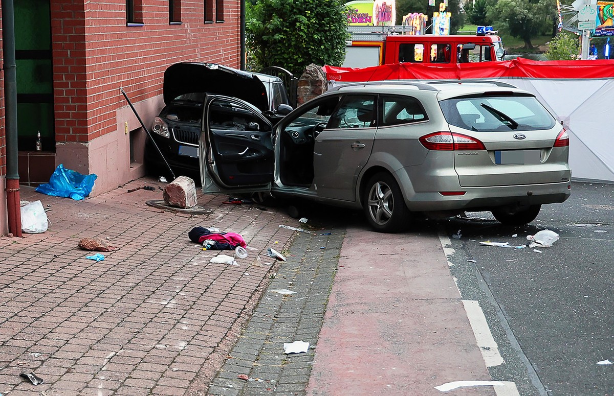 23.09.2024, Bayern, Großwallstadt: Zwei Fahrzeuge stehen im unterfränkischen Landkreis Miltenberg an der Unfallstelle. Ein Autofahrer ist auf der Kerb in eine Gruppe feiernder Menschen auf dem Fußweg ...