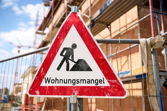 11 April 2024: Sign in front of a construction site of a residential building with the inscription: Housing shortage. Symbolic image of the real estate crisis. PHOTOMONTAGE *** Schild vor einer Bauste ...