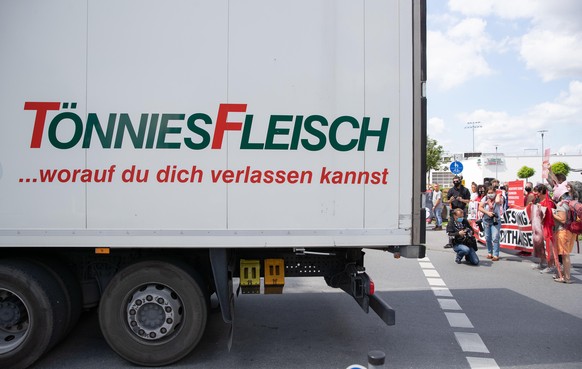 20.06.2020, Nordrhein-Westfalen, Rheda-Wiedenbrück: Demonstranten und Aktivisten, die gegen Tierquälerei demonstrieren, stehen vor dem Betriebsgelände der Fleischfabrik Tönnies, während ein Tönnies-La ...