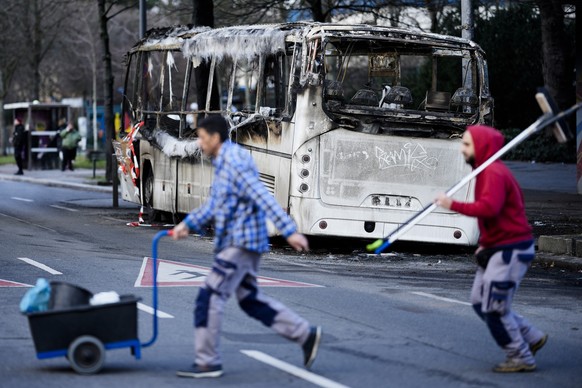 Two men cross the street in front of a burned-out bus standing beneath a residential building, in the district Neukoelln in Berlin, Germany, Tuesday, Jan. 3, 2023. People across Germany on Saturday re ...