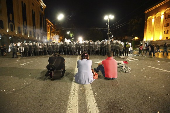 Three opposition demonstrators sit in front police line at Georgian Parliament as they gather to call for the resignation of the speaker of the Georgian Parliament in Tbilisi, Georgia, Friday, June 21 ...