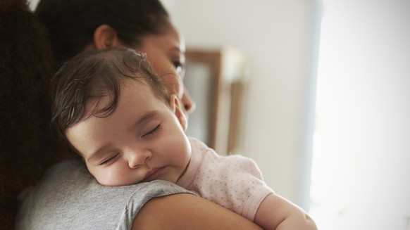 Close Up Of Mother Cuddling Sleeping Baby Daughter At Home