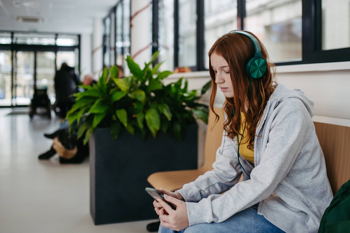 Teenage girl waiting in hospital corridor, listening music. Adolescent patient coming to hospital for examination. Teenage girl waiting in hospital corridor, listening music via headphones. Adolescent ...
