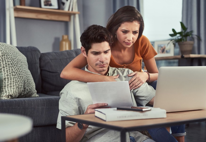 Shot of a young couple using a laptop while going through paperwork at home