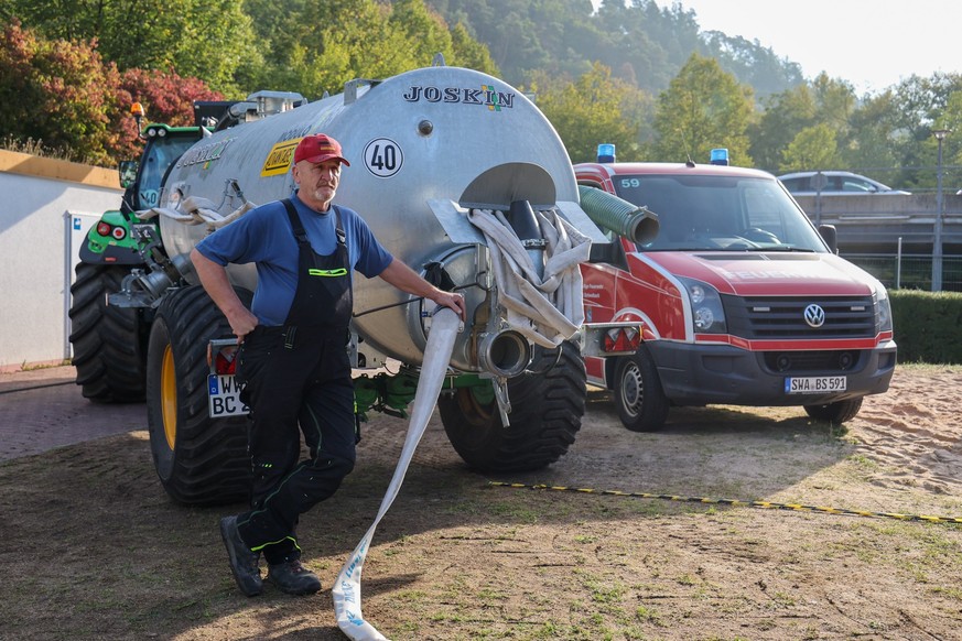 12.09.2022, Hessen, Bad Schwalbach: Benno Burggraf steht an seiner Zugmaschine mit Wassertank und bekommt mit einer Pumpe der Feuerwehr Wasser aus dem Becken, um anschließend die Bäume im Kurpark zu b ...