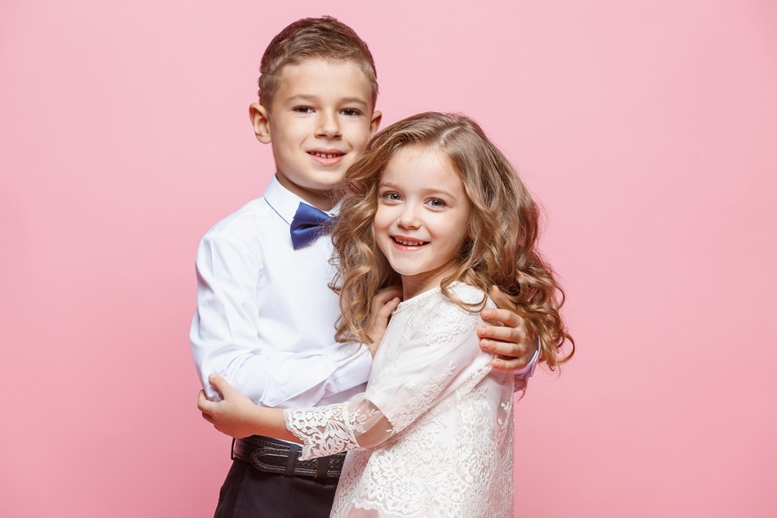 Boy and girl standing and posing in studio on pink background