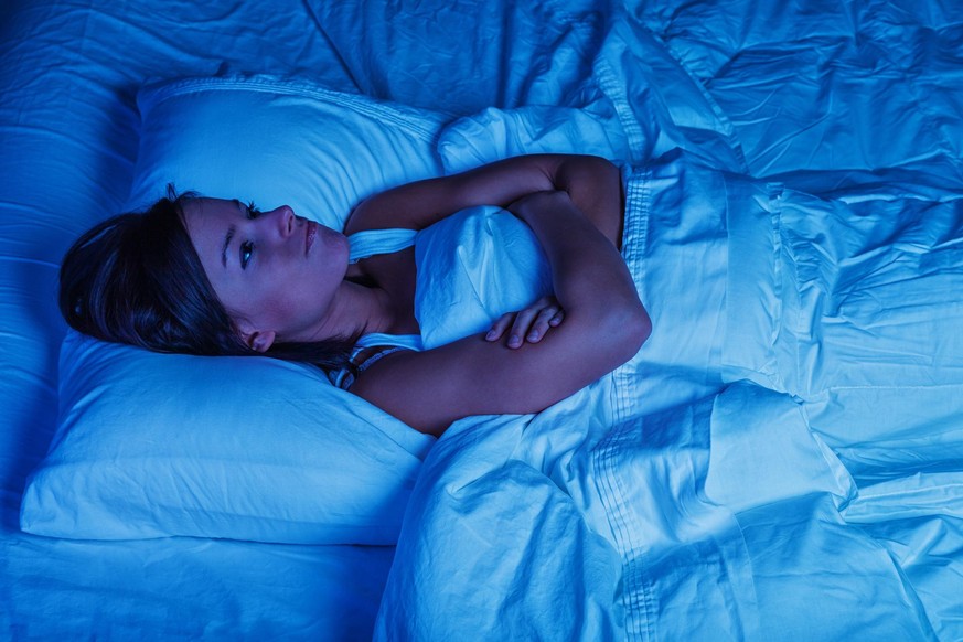 Photo of a young woman lying in bed at night, wide awake with a case of insomnia