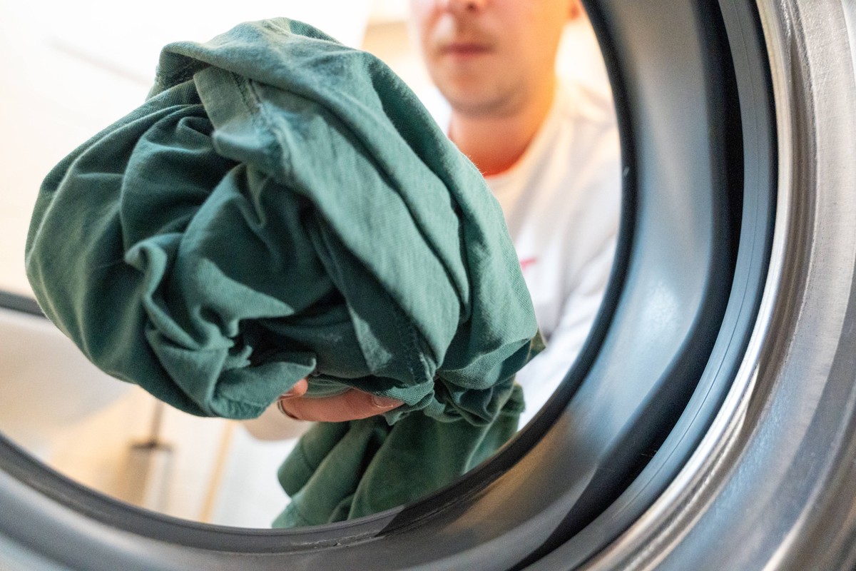 Bavaria, Germany - March 16, 2025: A person holds a bundle of laundry in front of a washing machine - a symbol of housekeeping, textile care and the importance of cleanliness in everyday life. Focus o ...