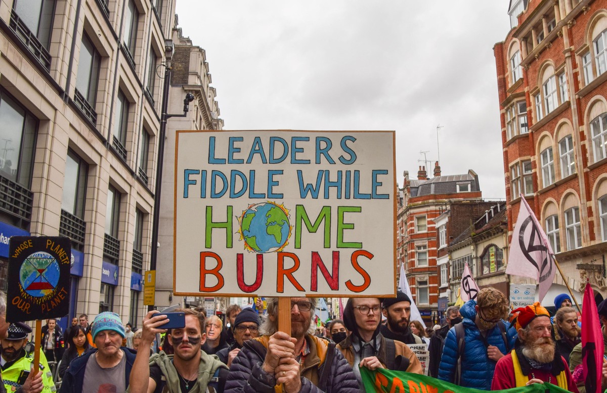 November 13, 2021, London, United Kingdom: A demonstrator holds a placard which says 'Leaders Fiddle While Home Burns' during the protest..Extinction Rebellion demonstrators marched through ...
