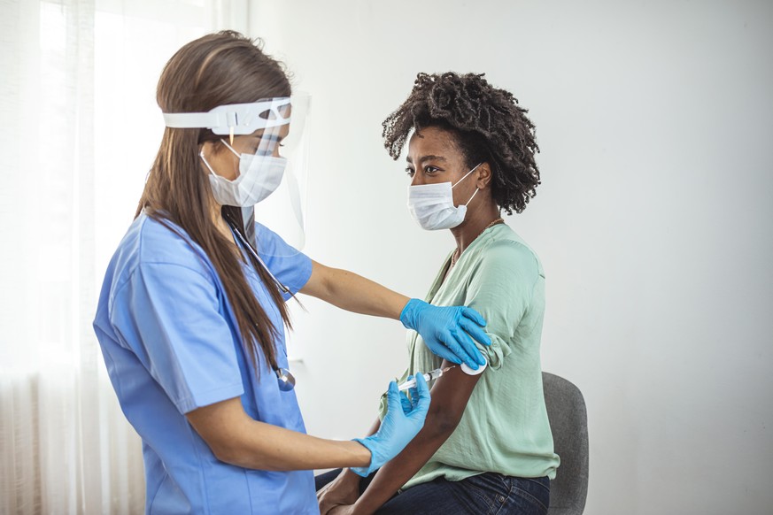 Vaccine and pandemics stills with people on a clinic environment. Covid-19 vaccination campaign concept with syringe applyed by doctor on a woman arm.