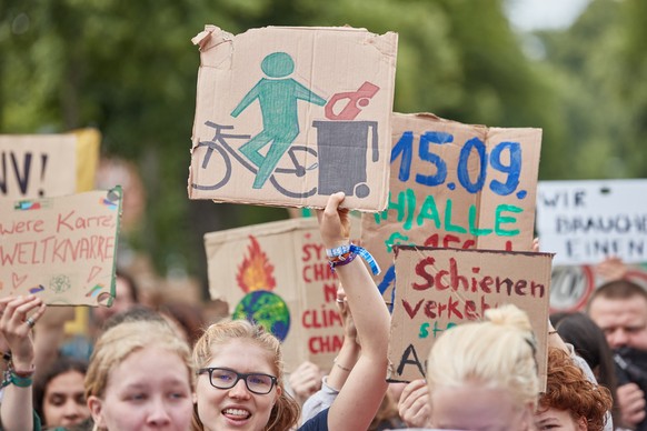 ARCHIV - 11.08.2023, Niedersachsen, L�neburg: Eine Teilnehmerin eines Protestzugs der Klimabewegung Fridays for Future tr�gt ein Pappschild mit einer Darstellung, auf der ein Radfahrer ein Auto in ein ...