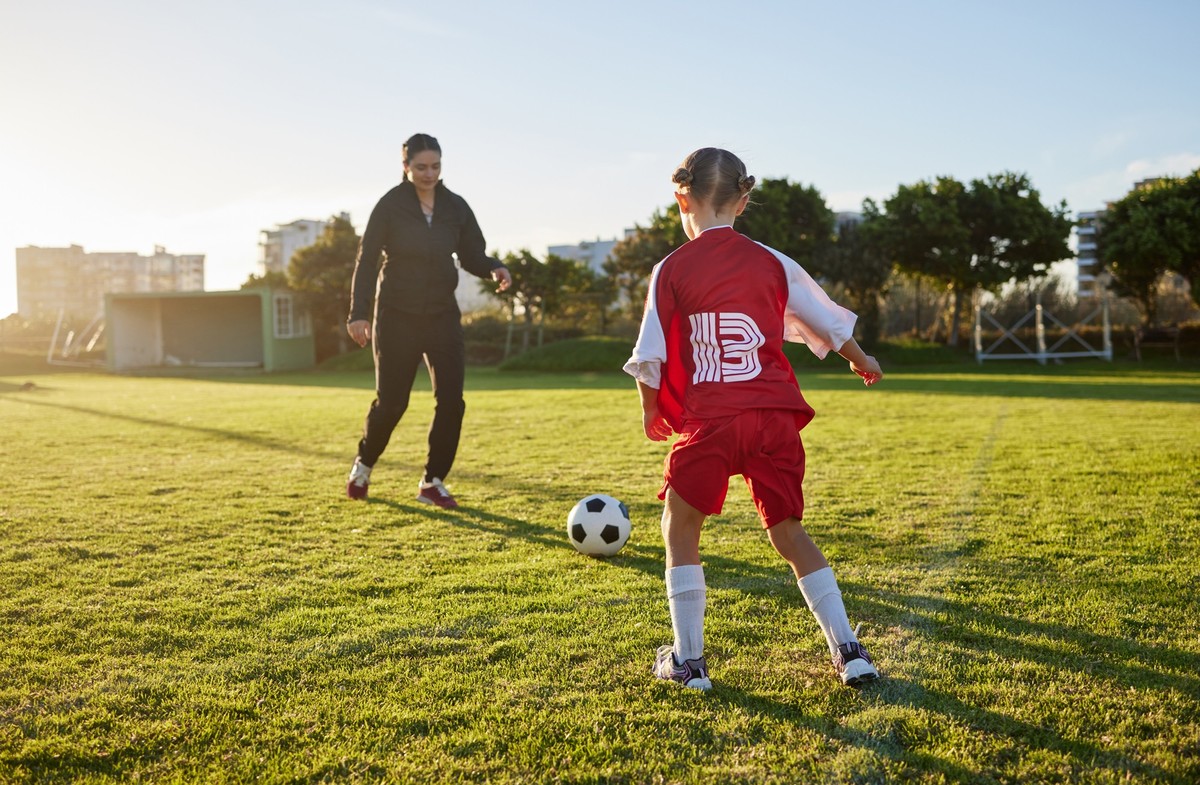 Soccer, coach mom and child sport on a outdoor school field with a ball for fitness and exercise. Mother training a kid student for football training, workout and children sports game kick together
