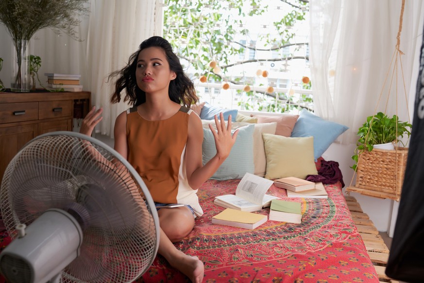 Sweating Asian girl cooling herself with big fan