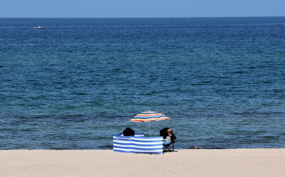 30.05.2023, Mecklenburg-Vorpommern, K�hlungsborn: Am Ostseestrand steht ein einzelner Windfang mit Sonnenschirm. Trotz Sonne ist es noch recht k�hl. Nach der vorl�ufigen Fr�hjahrs-Bilanz des Deutschen ...