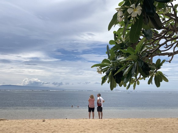 ARCHIV - 09.10.2022, Indonesien, Bali: Zwei Touristen stehen am Strand von Sanur. Die Tourismusbranche auf Bali ist besorgt �ber die von der indonesischen Regierung vorangetriebene massive Erh�hung de ...