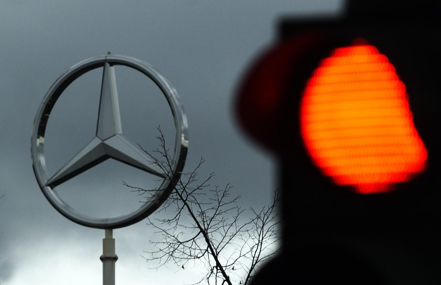 Dunkle Wolken ziehen über einen Mercedes-Stern, der auf dem Dach des Mercedes-Benz Sprinter - Werks steht. Daneben leuchtet eine Verkehrsampel rot. Laut Betriebsrat sollen bei Daimler weltweit 1100 St ...