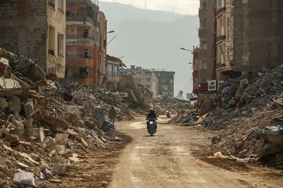 22.02.2023, Türkei, Samandag: Ein Mann fährt auf einem Motorrad an den Trümmern zerstörter Gebäude. Nach dem verheerenden Erdbeben am 06.02.2023 erschüttern weitere Nachbeben die Region. Foto: Emrah G ...