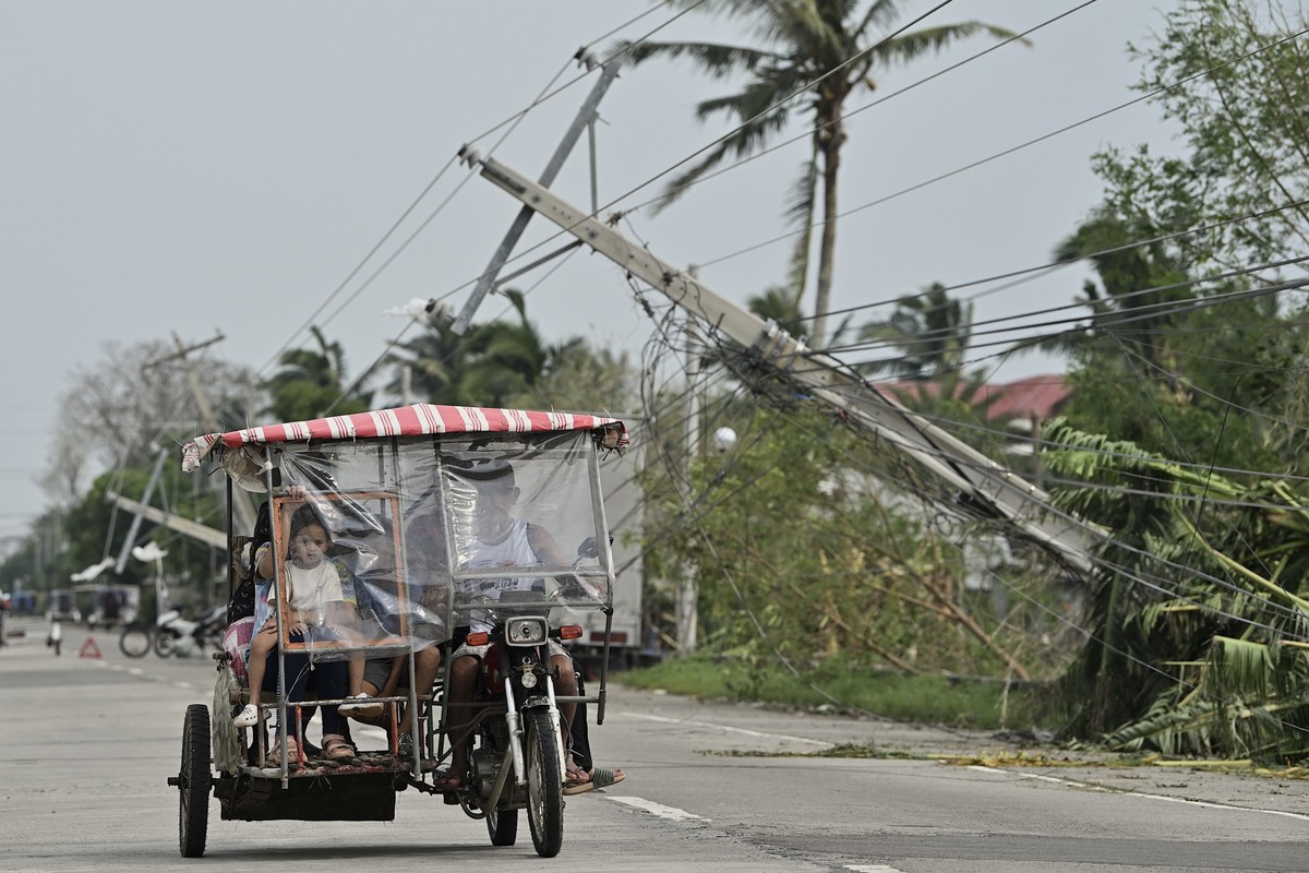 08.10.2024, Philippinen, Camalaniugan: Anwohner fahren auf einem Motorroller an umgestürzten Strommasten vorbei, nachdem der Taifun «Yinxing», lokal Marce genannt, auf Land traf. Foto: Noel Celis/AP/d ...
