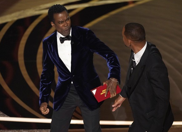 27.03.2022, USA, Los Angeles: Moderator Chris Rock (l) reagiert, nachdem er auf der Bühne von Will Smith eine Ohrfeige versetzt bekam, bei der 94. Verleihung der Academy Awards in Hollywood. Foto: Chr ...