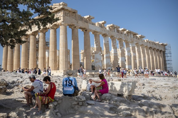 14.07.2023, Griechenland, Athen: Touristen ruhen sich an diesem heißen Tag bei ihrem Besuch des Parthenon-Tempels auf dem Akropolis-Hügel im Schatten aus. Das Kulturministerium hat beschlossen, die ar ...