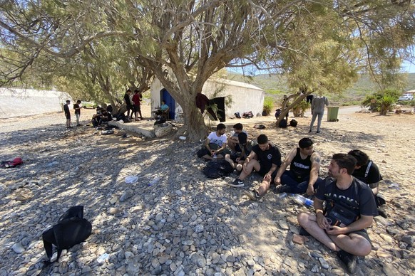 18.08.2022, Griechenland, Kythira: Migranten sitzen nach ihrer Ankunft auf der Insel am Strand unter B�umen. Am zweiten Tag in Folge sind Dutzende Migranten an Bord eines bootes au der Insel angekomme ...