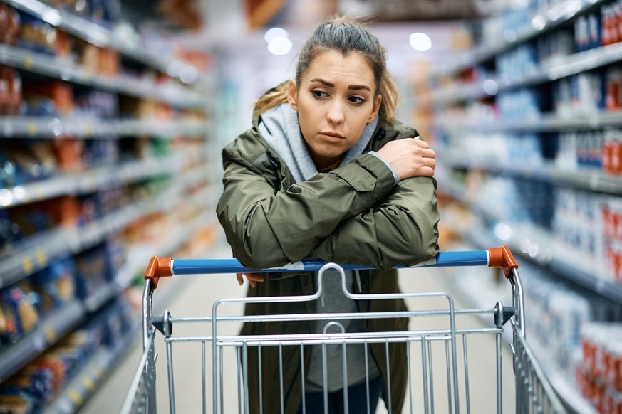 Young woman buying in supermarket and feeling worried about increase in food prices.