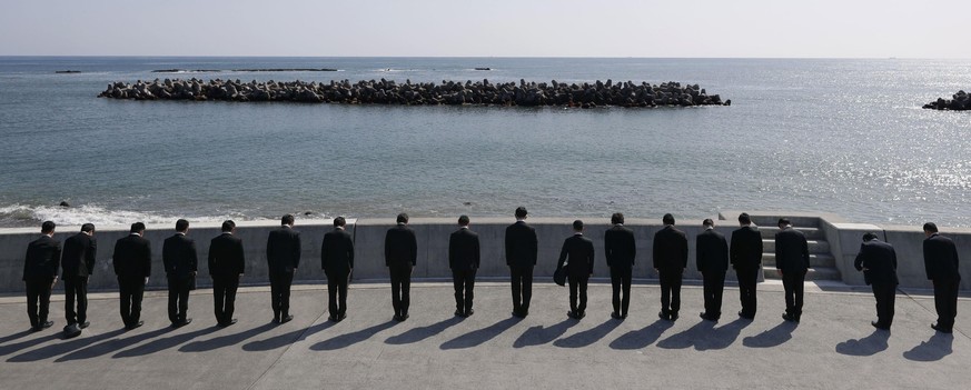 dpatopbilder - 11.03.2021, Japan, Iwaki: Menschen stellen sich mit Blick auf das Meer zu einer Schweigeminute in Iwaki, Pr