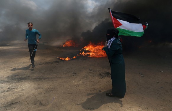 A woman holds a Palestinian flag as a demonstrator runs during a protest against U.S. embassy move to Jerusalem and ahead of the 70th anniversary of Nakba, at the Israel-Gaza border in the southern Ga ...