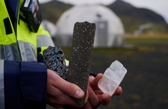 TOPSHOT - Thomas Ratouis, Head of Reservoir Engineering for Carbfix at the Hellisheidi power plant near Reykjavik, shows, a rock with unfilled pore (C), a rock with white dots is a core of basaltic ro ...
