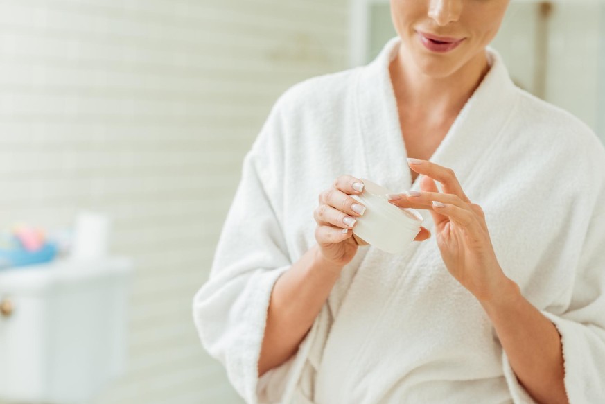 cropped shot of smiling young woman in bathrobe applying face cream