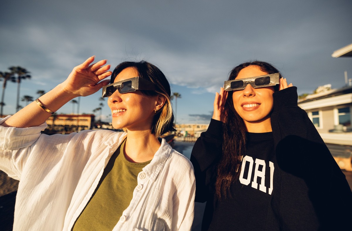 Two friends have fun together during a solar eclipse event. Their looking and pointing to the sun wearing the typical glasses normally used to watch a solar eclipse.