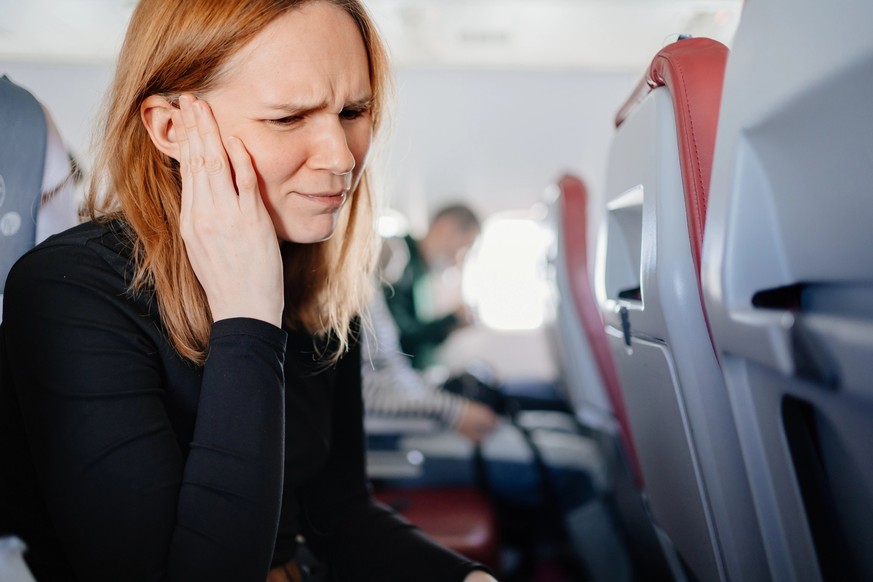 A woman sitting on an airplane has a headache and an earache while flying on an airplane. painkillers. first aid kit for travel.