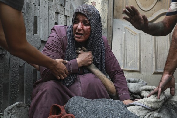 A wounded Palestinian woman cries as she holds the hand of her dead relative outside her home following Israeli airstrikes that targeted their neighborhood in Gaza City, Monday, Oct. 23, 2023. (AP Pho ...