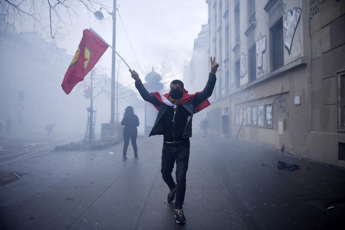24.12.2022, Frankreich, Paris: Ein Demonstrant h�lt eine Fahne der Kurdischen Arbeiterpartei (PKK) w�hrend eines Protestes nach Sch�ssen in einem Kulturzentrum in Paris. Bei Sch�ssen in einem kurdisch ...