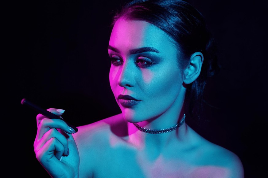 Portrait of glamour seductive gorgeous brunette woman smoking electronic cigarette in neon color light in studio