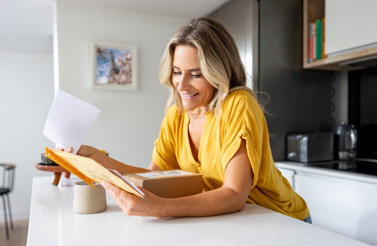 Happy woman at home checking her mail and receiving packages and letters - domestic life concepts