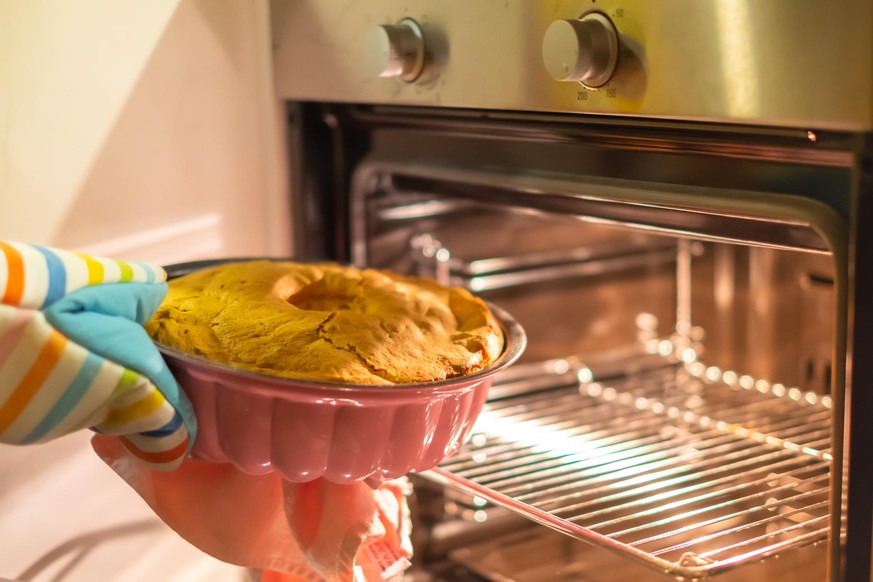 girl taking out the baked cake from oven with a towel