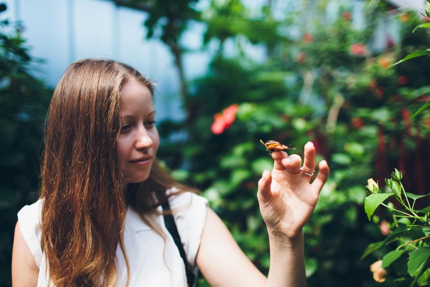 young woman with brown hair looking calm on the red and brown butterfly sitting on her hand