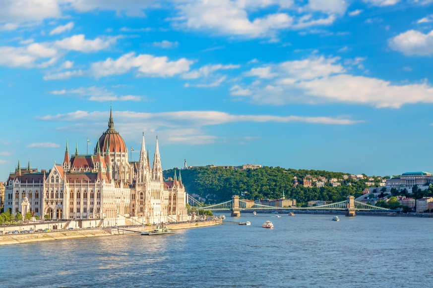 Travel and european tourism concept. Parliament and riverside in Budapest Hungary with sightseeing ships during summer sunny day with blue sky and clouds.
