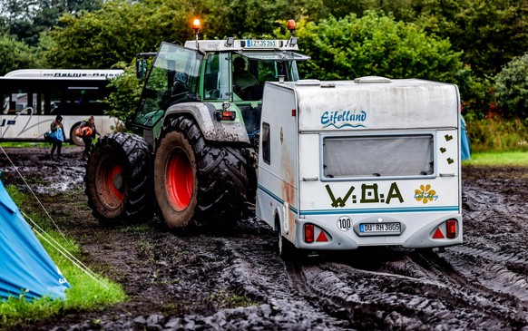 06.08.2023, Schleswig-Holstein, Wacken: Ein Traktor zieht einen Wohnwagen vom verschlammten Campinggelände des Wacken Open Air. Nach vier Tagen Heavy-Metal-Party verlassen zehntausende Metalfans den N ...