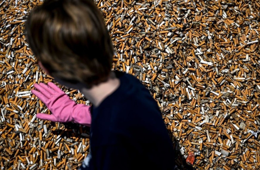A child dumps cigarette butts on a pile of them, collected in one week, at Comercio square in Lisbon on April 23, 2023. - Environmental activists gathered in one week around 650,000 cigarette butts an ...