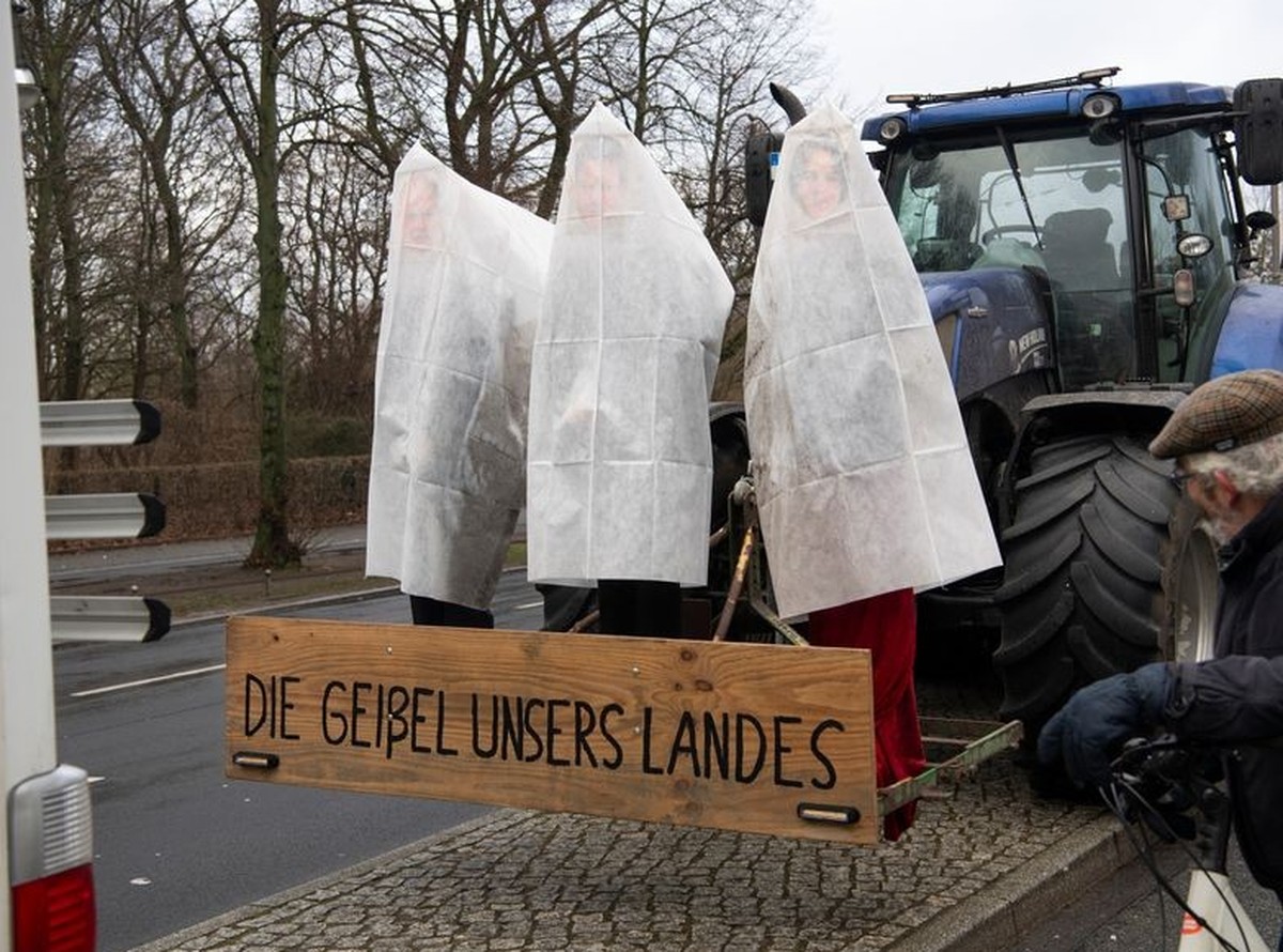 14.01.2024, Berlin: Verhüllte Figuren von Kanzler Scholz, Wirtschaftsminister Habeck und Außenministerin Berbock sind an einem Traktor auf der Straße des 17. Juni unweit des Brandenburger Tores zu seh ...