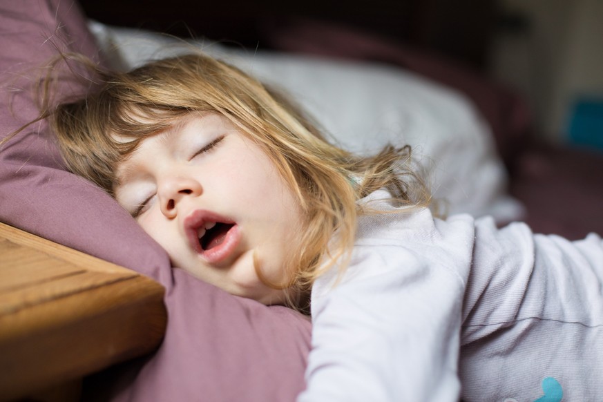 funny face expression with open mouth of blonde caucasian three years old child, sleeping on king bed