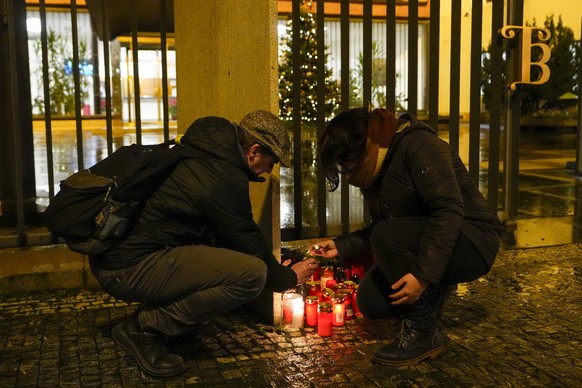 21.12.2023, Tschechien, Prag: Eine Frau entzündet Kerzen vor dem Gebäude der Philosophischen Fakultät der Karls-Universität in der Prager Innenstadt. Ein Schütze hat dort das Feuer eröffnet und viele  ...